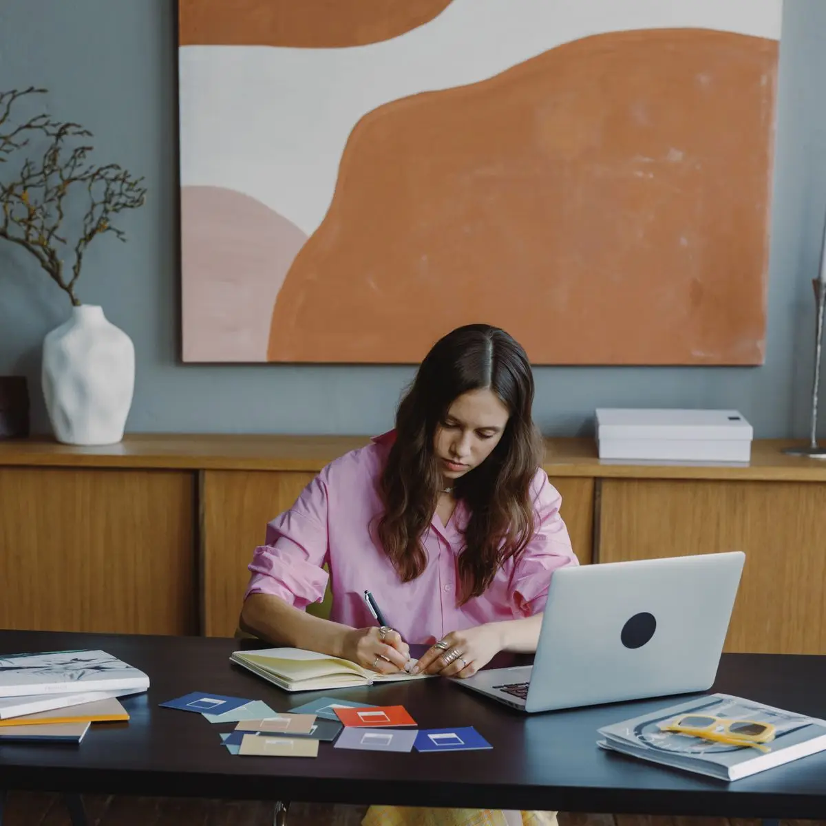 A designer at a studio desk comparing printed colour swatches beside a laptop